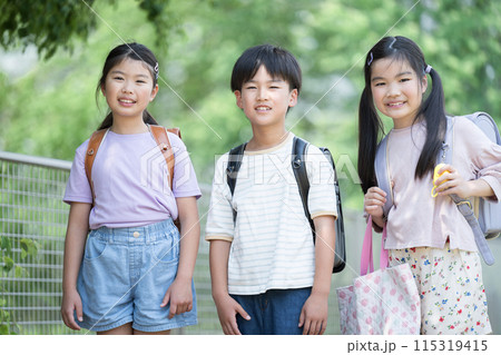 美しい新緑の中、ランドセルを背負った登校する小学生、仲良し同級生のカメラ目線 美しい新緑の中、ランドセルを背負った登校する小学生、仲良し同級生のカメラ目線 115319415