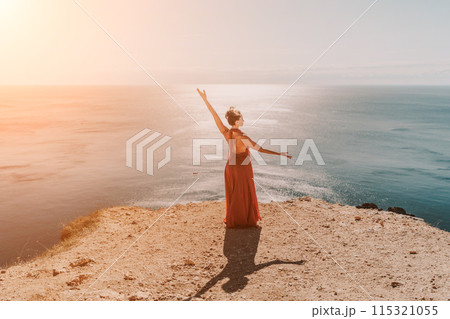 Woman red dress sea. Female dancer in a long red dress posing on a beach with rocks on sunny day. Girl on the nature on blue sky background. 115321055