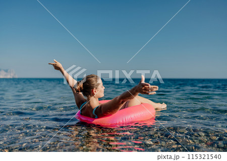 A woman is floating on a pink inflatable raft in the ocean A woman is floating on a pink inflatable raft in the ocean 115321540