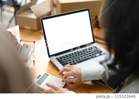 Small business owner sitting in front of laptop with blank screen and calculating expenses Small business owner sitting in front of laptop with blank screen and calculating expenses 115322648