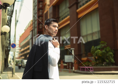 Handsome businessman walking in an urban street with jacket on shoulder Handsome businessman walking in an urban street with jacket on shoulder 115322715