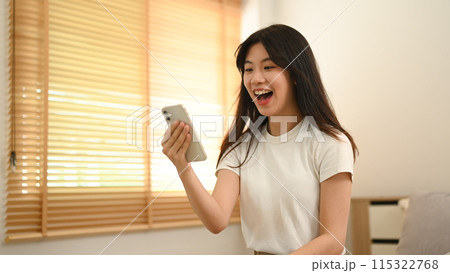 Pretty Asian woman looking at smartphone screen feeling surprise and excitedly 115322768