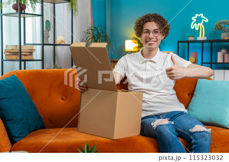 Happy customer man unpacking delivery parcel opening cardboard box receiving purchase gift at home 115323032