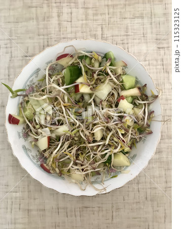 Salad of fresh vegetables and microgreens. Onions, apples, a mound of sprouted mung beans on a porcelain white plate on the table. Concept of diet, veganism, healthy foods. Close-up 115323125