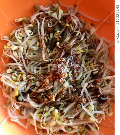 Salad of fresh sprouted mung beans microgreens with soy sauce in an orange bowl. Concept of diet, vegan, healthy products. Close-up 115323142