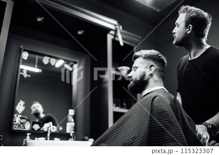 A man is getting his hair cut by another man in a barbershop A man is getting his hair cut by another man in a barbershop 115323307