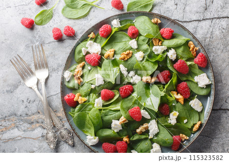 Vitamin delicious salad with raspberries, spinach, feta and walnuts with vinaigrette dressing close-up in a plate. Horizontal top view 115323582