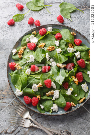 Summer salad of spinach, raspberries, feta and walnuts close-up in a plate. Vertical top view Summer salad of spinach, raspberries, feta and walnuts close-up in a plate. Vertical top view 115323585