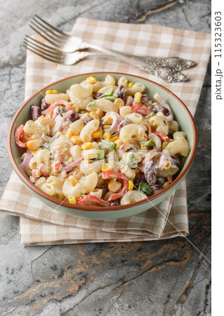 Southwestern pasta salad is a zesty summer side filled with fresh corn, onion, beans, peppers with creamy homemade ranch style dressing closeup on the bowl. Vertical 115323603