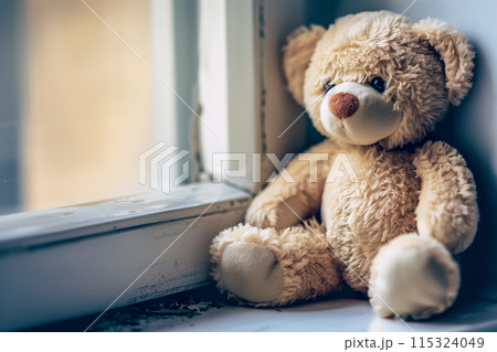 Plush toy seated by a sunlit window 115324049