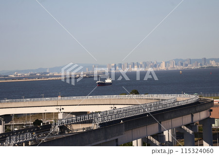 青空と高層ビルのある街並みと青い海面の海と大型船舶とモノレールの線路の見える人工島の風景 115324060