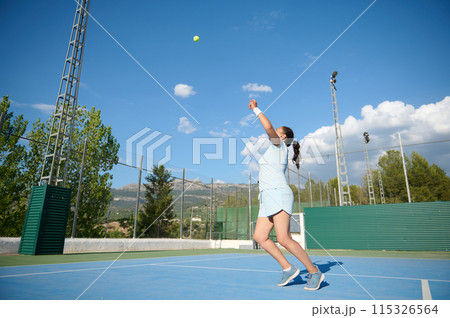 Woman playing tennis on outdoor court under a bright blue sky 115326564