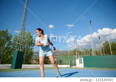Woman in her 40s playing tennis on an outdoor court under a clear sky 115326565