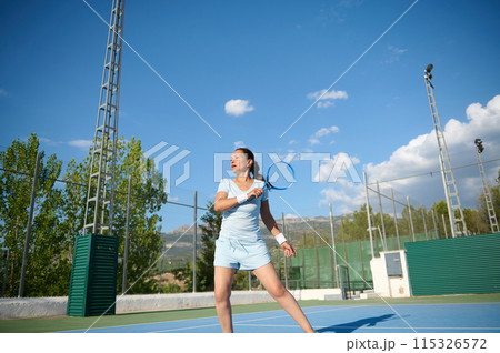 Middle-aged woman playing tennis on a sunny day at an outdoor court Middle-aged woman playing tennis on a sunny day at an outdoor court 115326572
