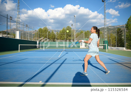 Woman in her 40s playing tennis on an outdoor court under a blue sky 115326584