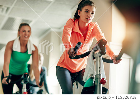 Woman, cycling and workout with spin class at gym for cardio exercise or indoor training together. Active female person or group of cyclists riding on equipment or bicycle for fitness at health club Woman, cycling and workout with spin class at gym for cardio exercise or indoor training together. Active female person or group of cyclists riding on equipment or bicycle for fitness at health club 115326718