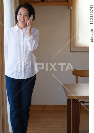 リビングで家族へ電話をするミドル女性 115326745