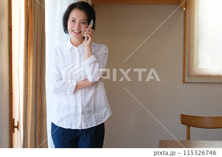 リビングで家族へ電話をするミドル女性 115326746