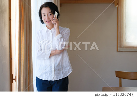 リビングで家族へ電話をするミドル女性 リビングで家族へ電話をするミドル女性 115326747