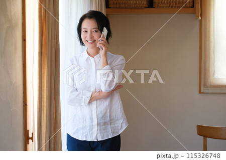 リビングで家族へ電話をするミドル女性 115326748
