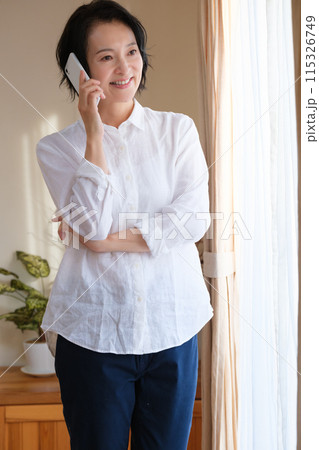 リビングで家族へ電話をするミドル女性 リビングで家族へ電話をするミドル女性 115326749