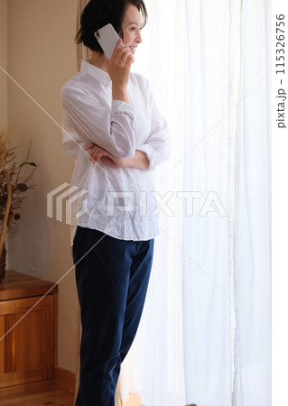 リビングで家族へ電話をするミドル女性 115326756