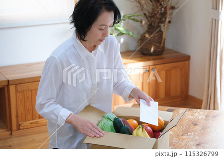 仕送りの段ボールに手紙を入れるミドル女性 仕送りの段ボールに手紙を入れるミドル女性 115326799