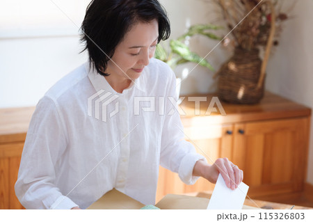 仕送りの段ボールに手紙を入れるミドル女性 115326803