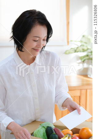 仕送りの段ボールに手紙を入れるミドル女性 115326806