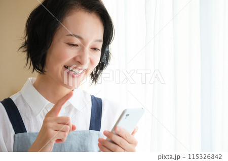 リビングでスマホを操作するミドル女性 115326842