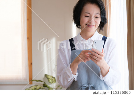 リビングでスマホを操作するミドル女性 115326860