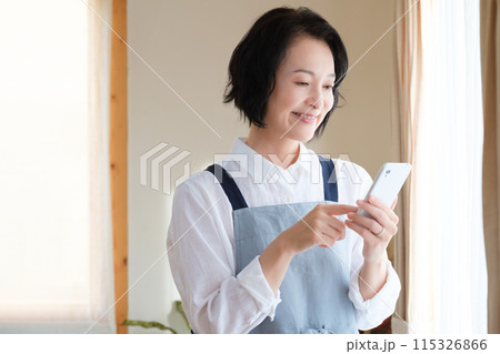 リビングでスマホを操作するミドル女性 115326866