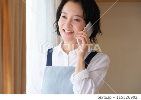 リビングで家族に電話をするミドル女性 リビングで家族に電話をするミドル女性 115326902