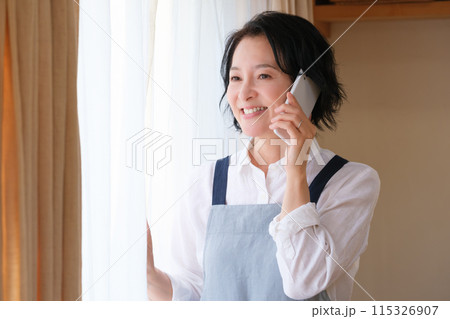 リビングで家族に電話をするミドル女性 リビングで家族に電話をするミドル女性 115326907