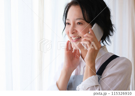 リビングで家族に電話をするミドル女性 115326910