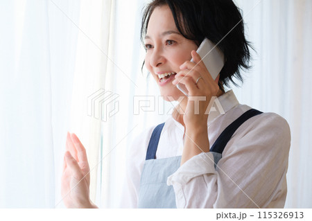 リビングで家族に電話をするミドル女性 115326913