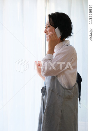 リビングで家族に電話をするミドル女性 115326914