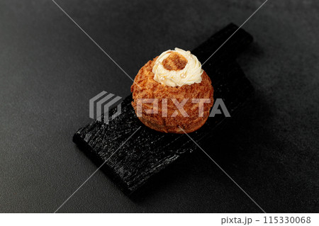 Classic Shu cake (choux). Custard dough based on butter and milk, classic custard filling with added cream on a black cutting board Classic Shu cake (choux). Custard dough based on butter and milk, classic custard filling with added cream on a black cutting board 115330068