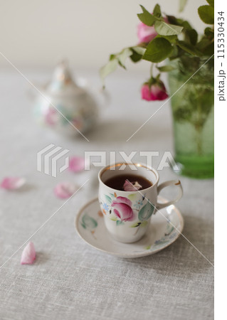 Moody summer still life. Table composition with cup of coffee, tea and beautiful floral bouquet with pink roses 115330434