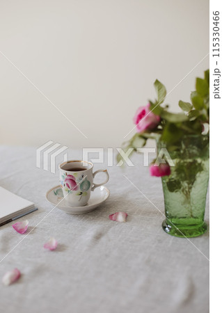 Moody summer still life. Table composition with cup of coffee, tea and beautiful floral bouquet with pink roses Moody summer still life. Table composition with cup of coffee, tea and beautiful floral bouquet with pink roses 115330466