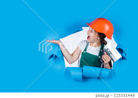 cheerful child laborer using building uniform and tool, presenting product on copy space, service 115331449