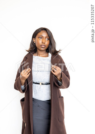Confident woman in professional attire wears a brown coat with a serious expression, at work Confident woman in professional attire wears a brown coat with a serious expression, at work 115335207