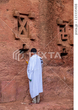 Man in white cloak praying at the walls of rock hewn monolithic ortodox church of Bete Maryam, Lalibela, Amhara Region, Ethiopia. Man in white cloak praying at the walls of rock hewn monolithic ortodox church of Bete Maryam, Lalibela, Amhara Region, Ethiopia. 115335408