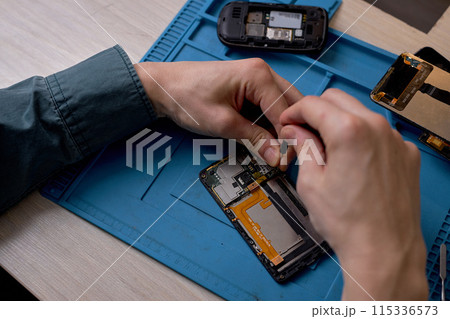 top view on repairman's hands unscrewing screws from smartphone case with screwdriver 115336573