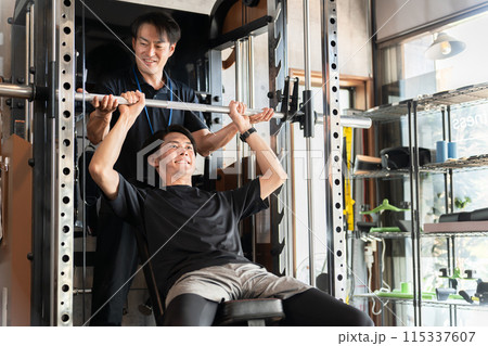 ジムでパーソナルトレーニングを受ける男性とトレーナー・インストラクターの男性 ジムでパーソナルトレーニングを受ける男性とトレーナー・インストラクターの男性 115337607