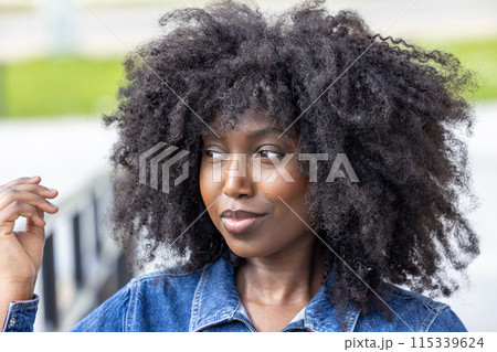 Stylish woman with curly hair in denim jacket exuding confidence and charm in urban setting 115339624