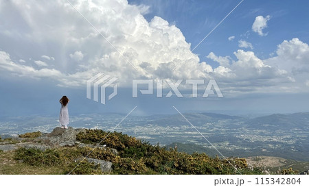 on the highest mountain in Portugal stands a girl her hair blows in the wind standing on top of the mountain relaxing and enjoying beautiful summer mountain landscape. A panoramic view  115342804