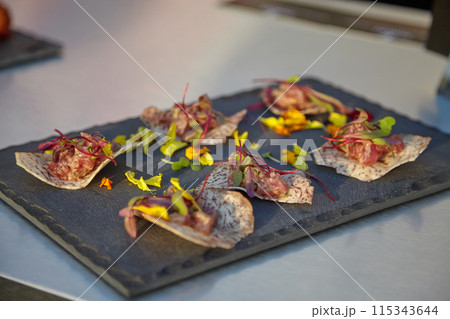 Appetizers on a slate plate with edible flowers and herbs offer a sophisticated dining experience 115343644