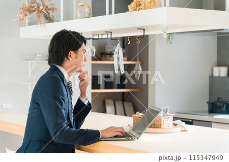 自宅のダイニングテーブルで仕事をするスーツ姿の若いアジア人ビジネスマン 自宅のダイニングテーブルで仕事をするスーツ姿の若いアジア人ビジネスマン 115347949