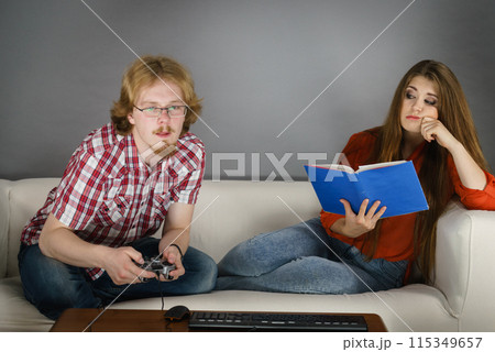 Woman playing games man reading book Woman playing games man reading book 115349657
